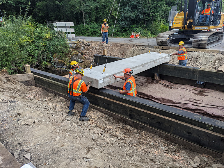 Six crew members to set the first of several concrete slabs for the new Clough Creek bridge deck.