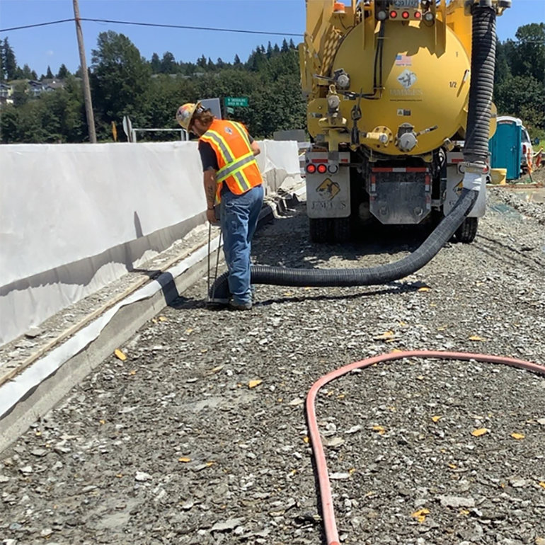 A crewmember uses a large hose to vacuum the debris after hydrodemolition. 