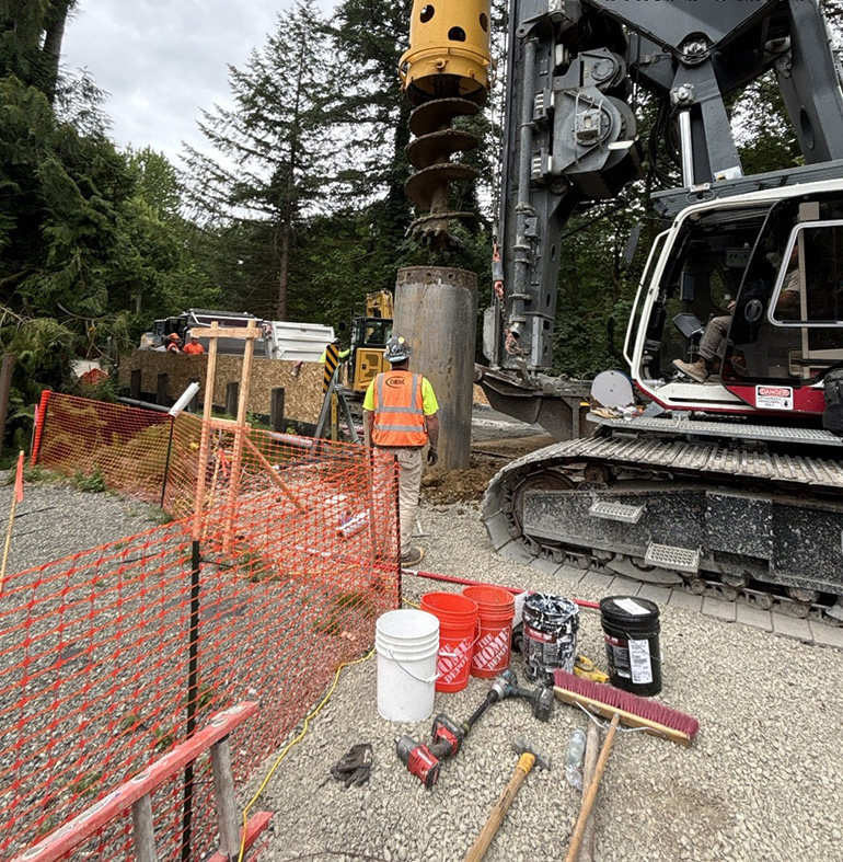 Heavy machinery drill in ground and construction worker.