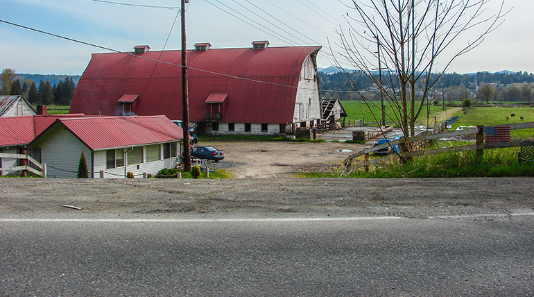 Raod passing white barn with red roof