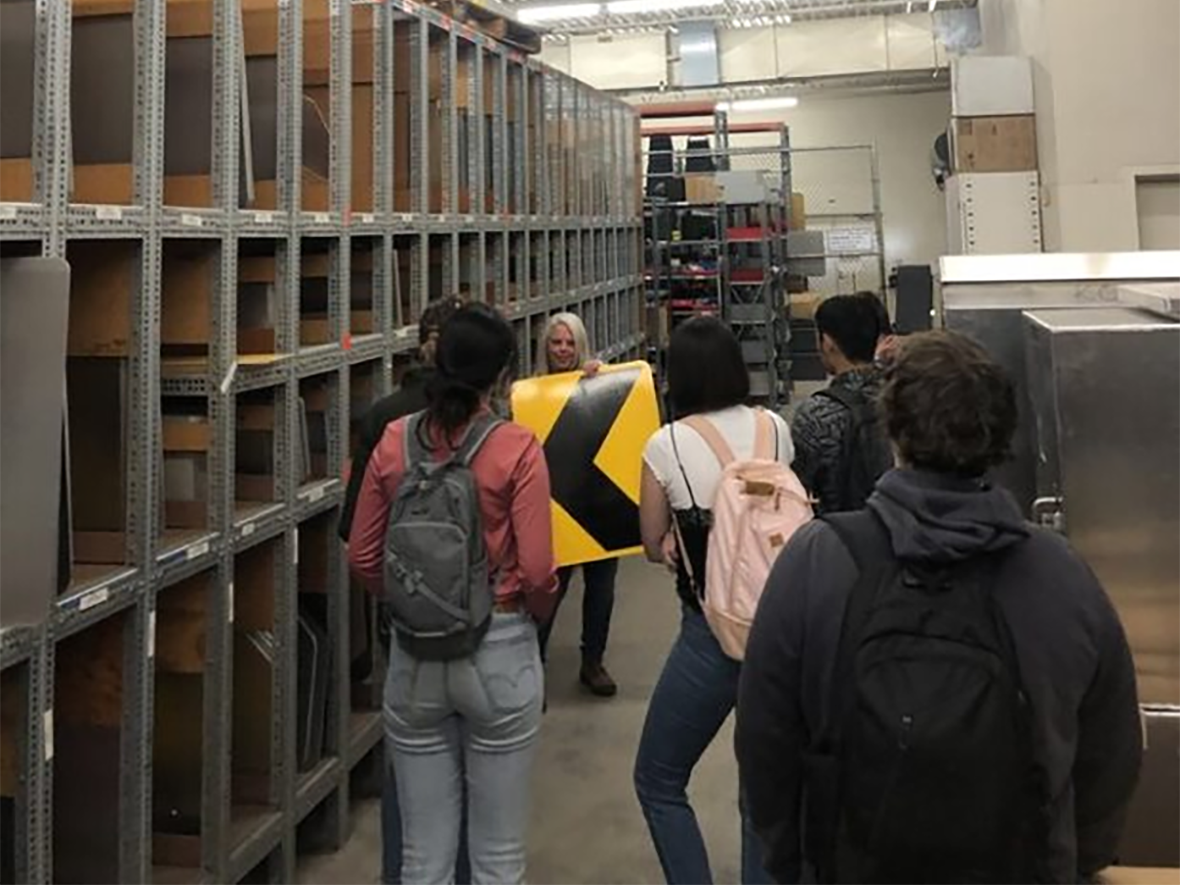 Interns on a tour of the sign shop looking at the area where signs are stored.