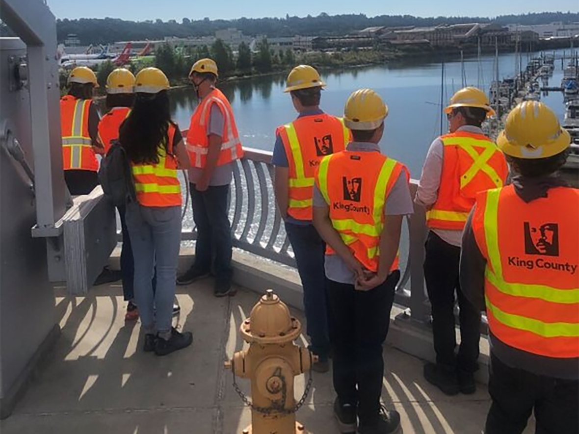Interns visiting the South Park Bridge standing outside looking at the Duwamish River.