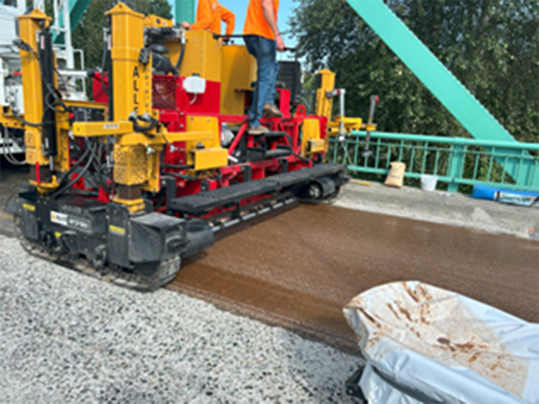 Heavy machinery facilitates polyester polymer concrete application on a bridge.