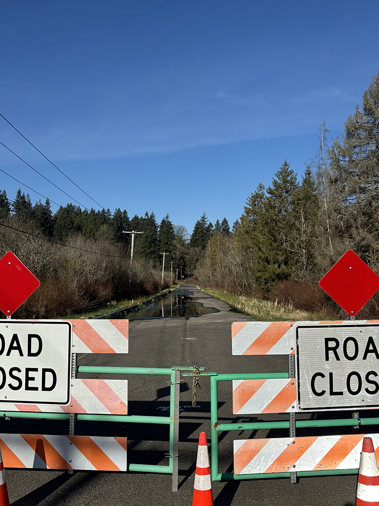 Road closed barricades blocking road with water over it.