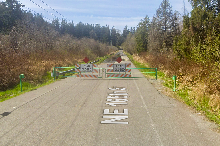 NE 165th St Road with Road Closed signs on Green gates. Water over the roadway can be seen in distance.