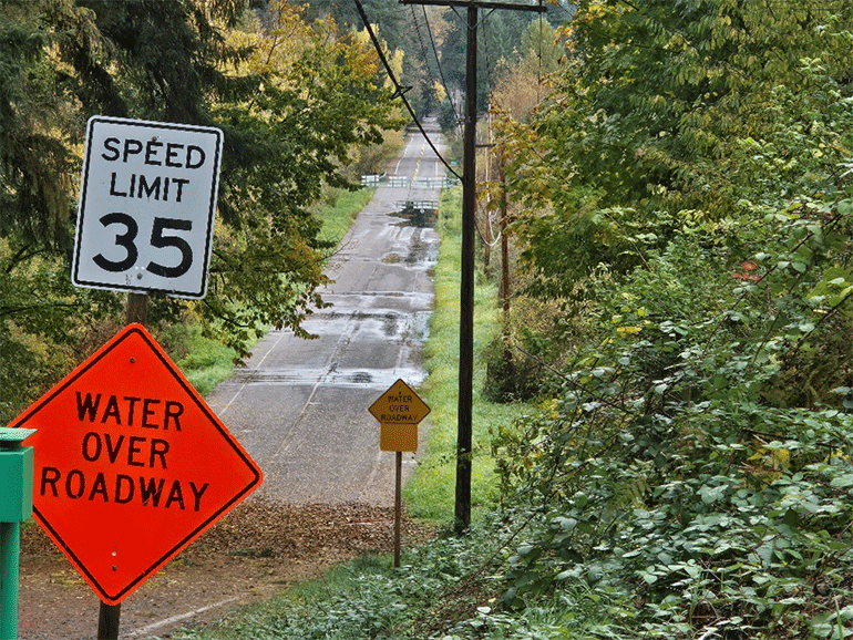 Orange water over roadway sign in front of NE 179th Place, water can be seen over the road. 