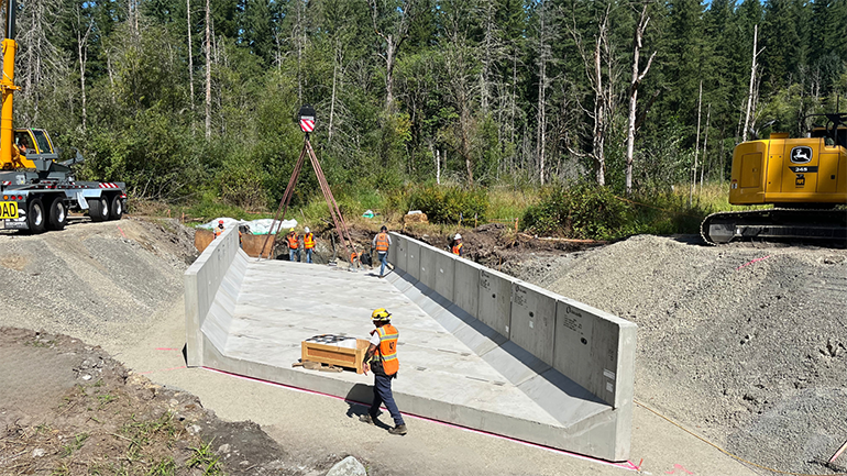 Using a large crane, crews carefully lift and place prefabricated panels of the bottom and sides of the new box culvert into place. 