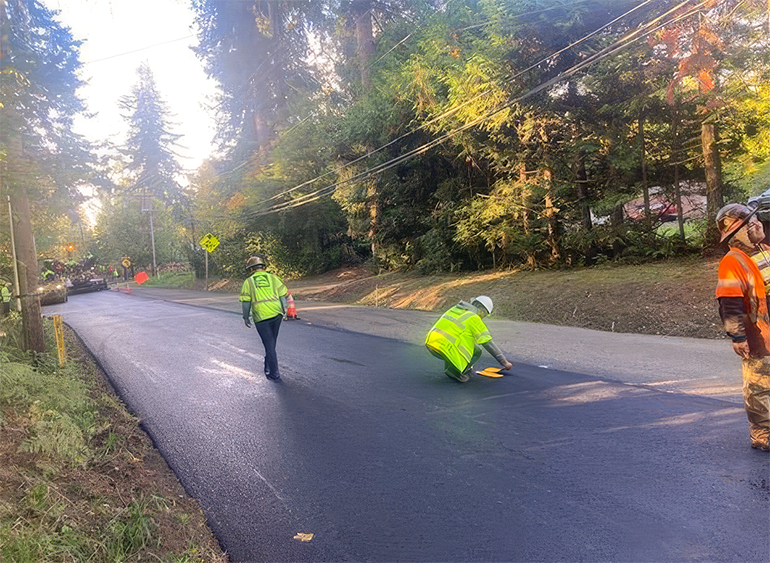 Crew workers on fresh asphalt installing yellow reflective tape