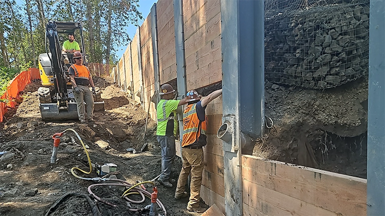 Crew members place timber beams in between soldier piles.