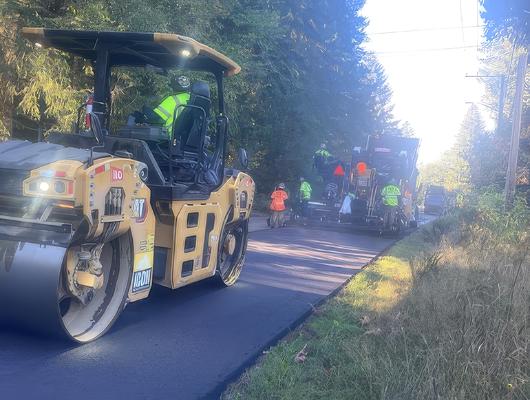 Crew workers laying fresh asphalt with heavy machinery