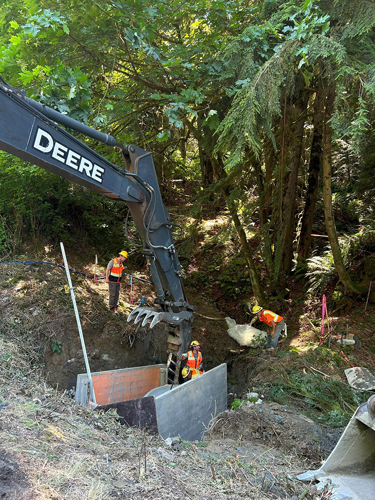 Crews guided a large concrete cylinder into position below the road.
