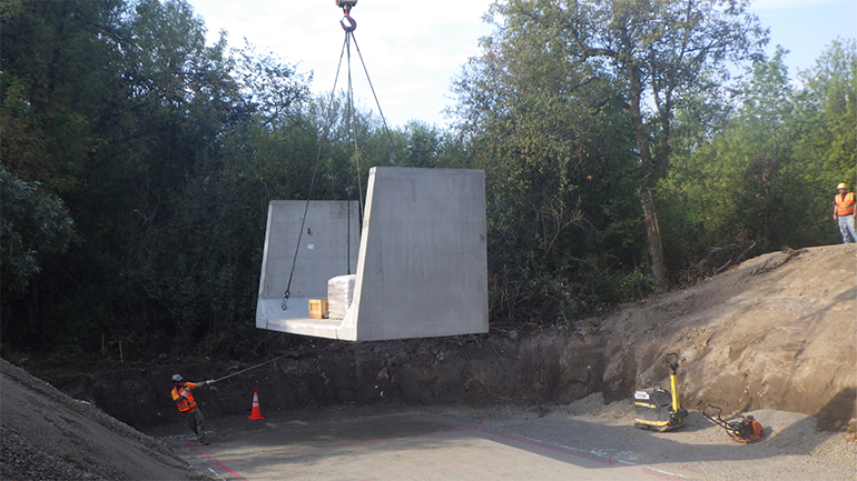 Using a crane, a member of the crew pulls the first section of the bottom of the new concrete box culvert into place. 