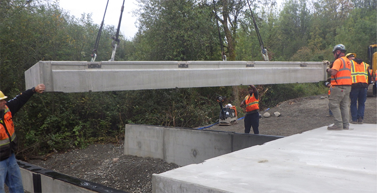 Using a crane, crew members guide the lid of the culvert into place.
