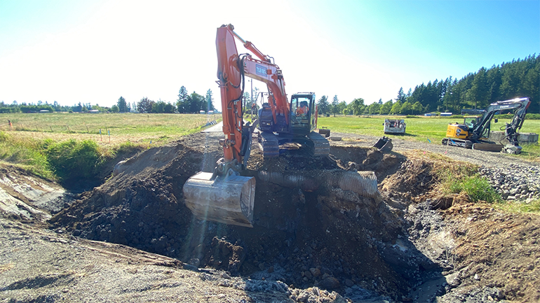 Heavy machinery scrapes away at the earth to remove the old, rusted pipe.