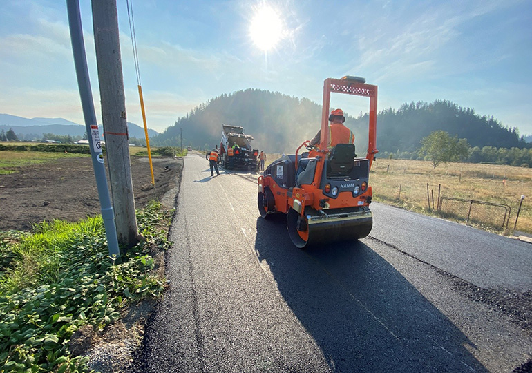 Construction workers smoothing over a fresh layer of asphalt with heavy machinery.