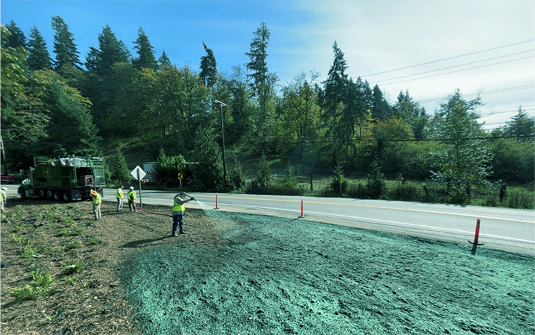 Crew workers spraying grass seed on hilsside on a sunny day