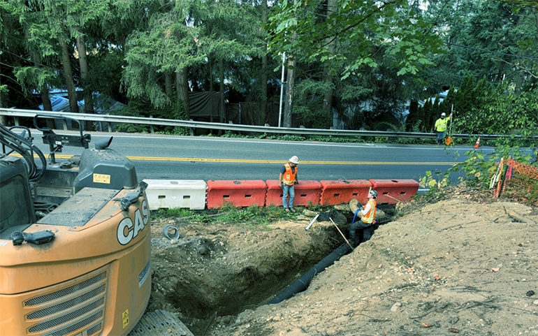 Crew workers in new catch basin along side of road with construction barriers.