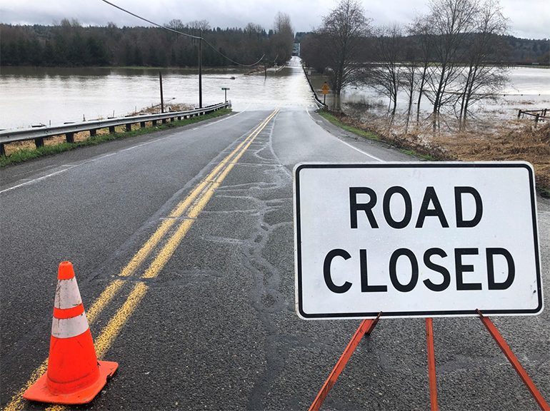 Flooded road in unincorporated King County with road closure sign and traffic cone.