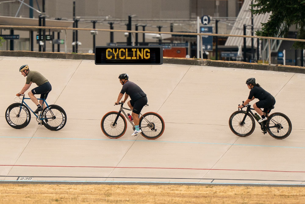 A group of cyclists race along a velodrome with large wooden curved walls around them.
