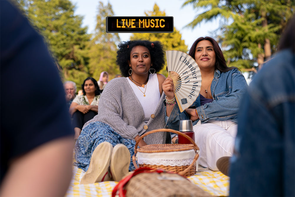 Two young adults enjoy a picnic while watching a chamber music concert in the park.