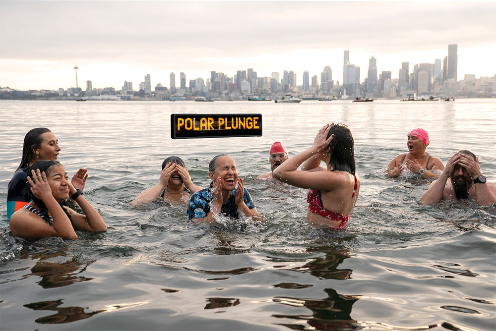 A group of people jump into the Puget Sound as the West Seattle Water Taxi floats behind them.