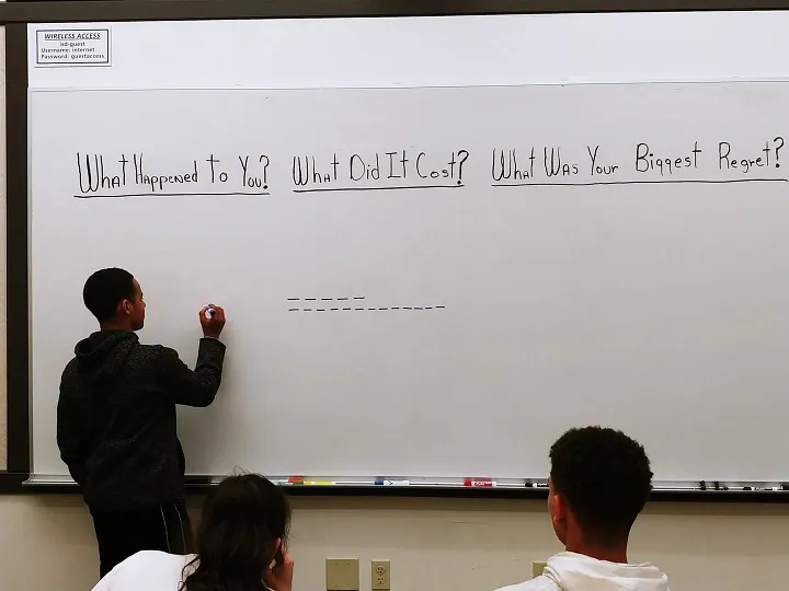 A photo of a child responding to prompts about detailing their goals on a whiteboard in front of others at an Education & Reengagement Workshop at Redmond Community Center.