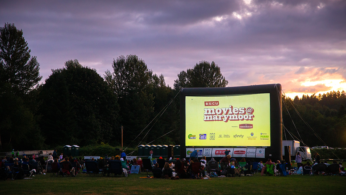 Movie night at Marymoor outdoor theater with sun setting and movie goers watching the big screen from a grassy field