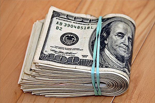 Folded wad of hundred dollar bills on a wood table