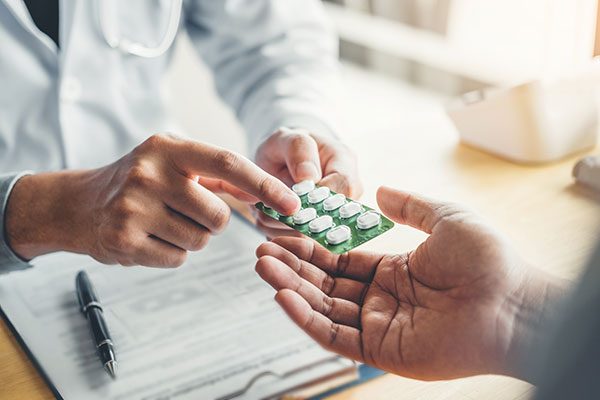 Closeup on a pair of hands handing another person a pack of pills across a desk.