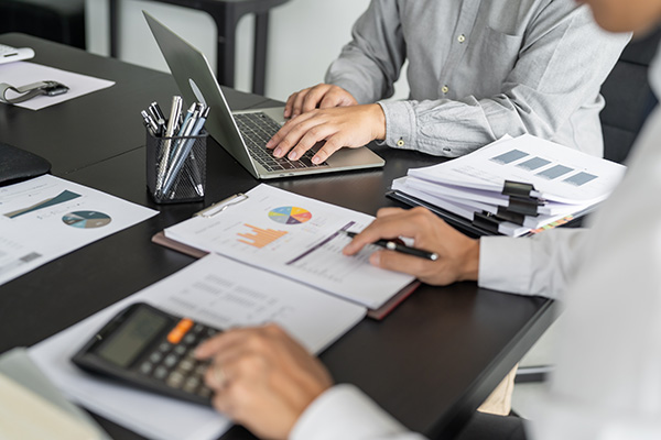 Closeup of conference room tabletop with two sets of hands, a laptop, calculator, and papers