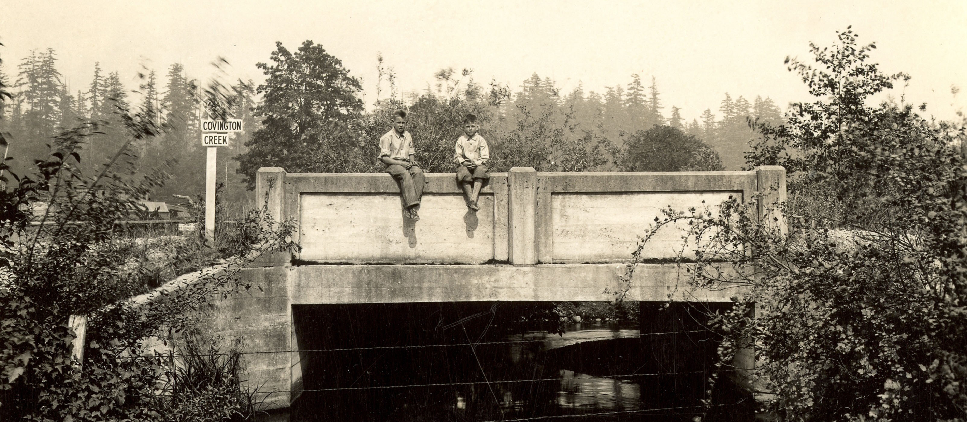 Two boys sitting on the edge of a concrete bridge